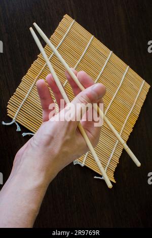 Stäbchen in der Hand auf dem Hintergrund einer Sushi-Matte Stockfoto