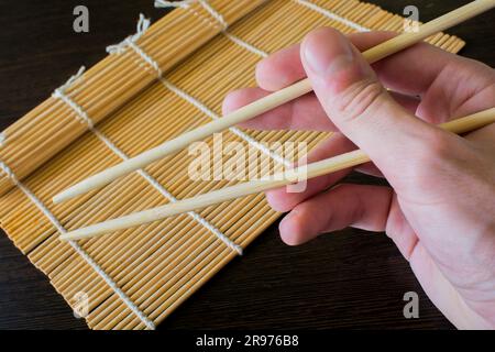 Stäbchen in der Hand auf dem Hintergrund einer Sushi-Matte Stockfoto