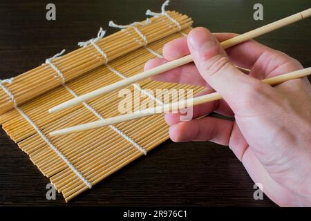 Stäbchen in der Hand auf dem Hintergrund einer Sushi-Matte Stockfoto
