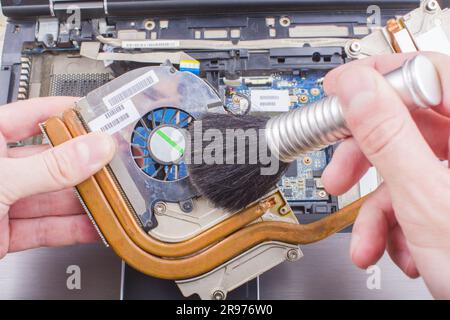 Man reinigt die Kühlanlage des Laptopkühlers mit einer Bürste vom Staub, Nahaufnahme Stockfoto