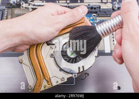 Man reinigt die Kühlanlage des Laptopkühlers mit einer Bürste vom Staub, Nahaufnahme Stockfoto