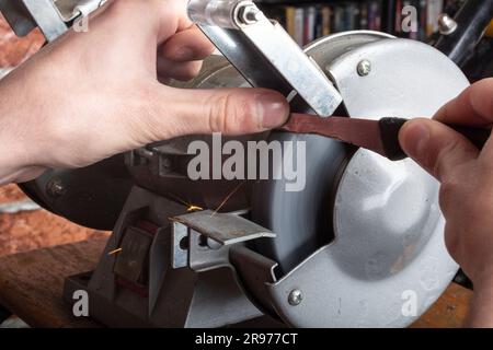 Ein Messerschärfer und eine Hand mit Klinge auf einem Holztisch, Nahaufnahme vor einem Backsteinhintergrund Stockfoto
