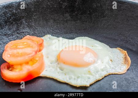 Gebratenes Ei mit gehackten Tomaten in einer gusseisernen Bratpfanne auf einem Holztisch Stockfoto