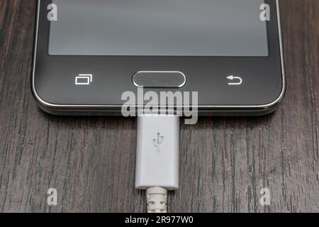 Mobile Smartphones laden ein weißes Kabel auf einem Holztisch Stockfoto