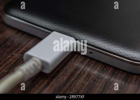 Mobile Smartphones laden ein weißes Kabel auf einem Holztisch Stockfoto