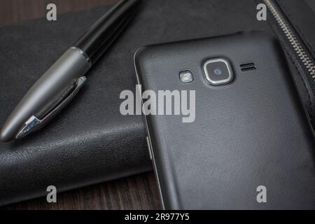 Telefon mit Stift und Handtasche liegen auf einem Holztisch Stockfoto