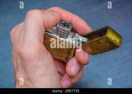 Hand gehalten goldenes Klappheller auf einem dunklen Hintergrund in gelb-blauen Tönen Wärme der Kälte Stockfoto