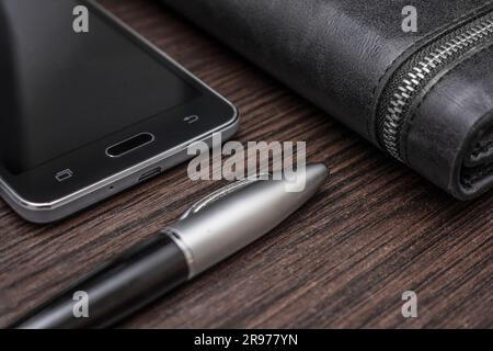 Telefon mit Stift und Handtasche liegen auf einem Holztisch Stockfoto