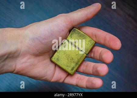 Hand gehalten goldenes Klappheller auf einem dunklen Hintergrund in gelb-blauen Tönen Wärme der Kälte Stockfoto