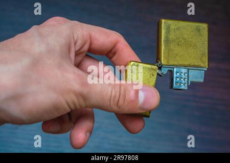 Hand gehalten goldenes Klappheller auf einem dunklen Hintergrund in gelb-blauen Tönen Wärme der Kälte Stockfoto