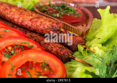 Gebratene Kebab-Lilie auf einem Salat mit Tomaten und Dill mit Petersilie auf einem Baum vor einem Backsteingebäude Stockfoto