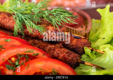 Gebratene Kebab-Lilie auf einem Salat mit Tomaten und Dill mit Petersilie auf einem Baum vor einem Backsteingebäude Stockfoto