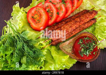 Gebratene Kebab-Lilie auf einem Salat mit Tomaten und Dill mit Petersilie auf einem Baum vor einem Backsteingebäude Stockfoto