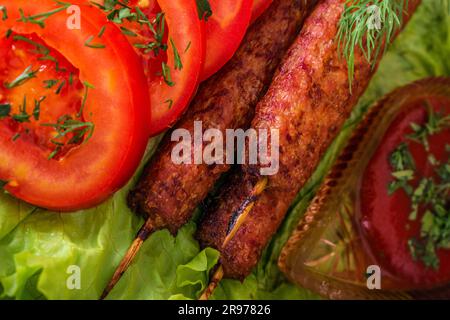 Gebratene Kebab-Lilie auf einem Salat mit Tomaten und Dill mit Petersilie auf einem Baum vor einem Backsteingebäude Stockfoto