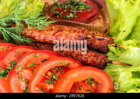 Gebratene Kebab-Lilie auf einem Salat mit Tomaten und Dill mit Petersilie auf einem Baum vor einem Backsteingebäude Stockfoto