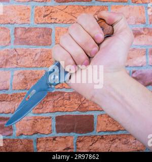 Klappmesser in männlichen Händen, vor dem Hintergrund einer orangefarbenen Mauer Stockfoto