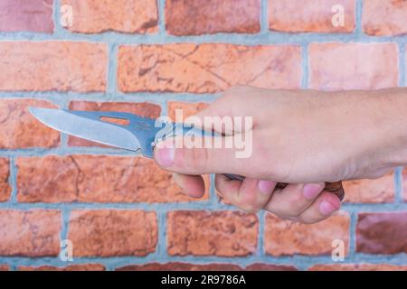 Klappmesser in männlichen Händen, vor dem Hintergrund einer orangefarbenen Mauer Stockfoto