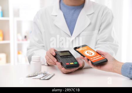 Frau, die das Terminal für kontaktlose Bezahlung mit Smartphone in der Apotheke, Nahaufnahme verwendet. Bildschirm „Transaktion abgeschlossen“ auf dem Gerät Stockfoto