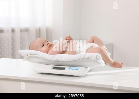 Niedliches kleines Baby, das in der Klinik auf einer Waage liegt Stockfoto