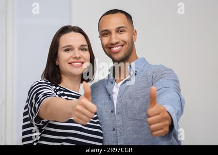 Dating-Agentur. Glückliches Paar, das Daumen nach oben zeigt, nahe der weißen Wand Stockfoto