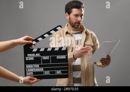 Schauspieler, während zweite Kamera Klapptafel auf grauem Hintergrund hält Stockfoto