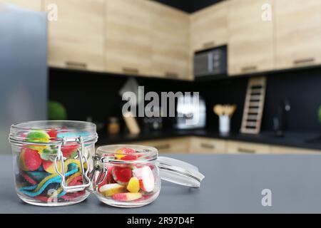 Glasgefäße mit leckeren Gummibonbons auf einem grauen Tisch in der Küche. Platz für Text Stockfoto