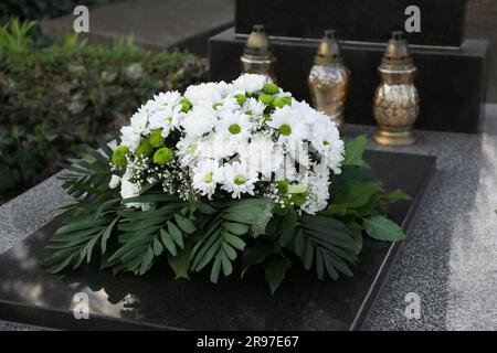 Bestattungskranz aus Blumen und Grablaternen auf Granitgräberstein auf dem Friedhof Stockfoto