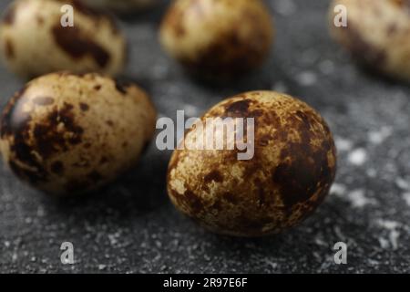 Viele gesprenkelte Wachteleier auf einem schwarz strukturierten Tisch, Nahaufnahme Stockfoto