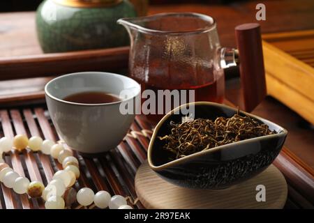 Aromatischer Dianhong-Tee und Gebetsperlen auf Holztablett, Nahaufnahme. Traditionelle Zeremonie Stockfoto