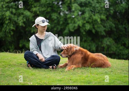Der Golden Retriever-Hund sitzt mit dem Besitzer auf dem Gras Stockfoto