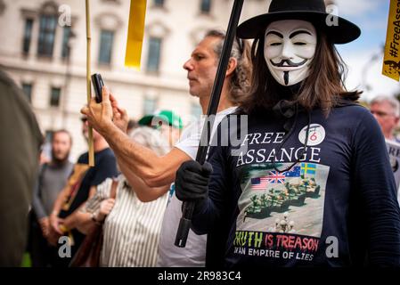 Ein maskierter Demonstrant nimmt an der "irgendwas zu sagen?" Teil. Freier Julian Assange-Protest am Parliament Square in London. „Haben Sie Etwas Zu Sagen?“ Ist eine lebensgroße Bronzeskulptur, in der jeweils drei Figuren dargestellt werden, die auf einem Stuhl des Künstlers Davide Dormino stehen. Der vierte Stuhl ist leer, weil er unser Stuhl ist. Der, auf dem wir uns erheben, um uns auszudrücken oder einfach nur neben Edward Snowden, Julian Assange und Chelsea Manning zu stehen, die den Mut hatten, Nein zu der Einmischung in die globale Überwachung und zu Lügen zu sagen, die zu Krieg führten. Stockfoto