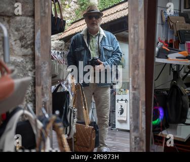 Kotor, Montenegro, 13. April 2023: Ein Fotograf mit Hut steht neben Verkaufsständen auf dem Straßenbasar in der Altstadt Stockfoto