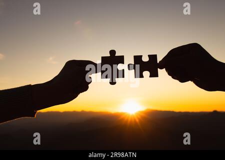 Geschäftskonzept: Silhouette von Mann und Frau hält bei Sonnenuntergang ein Puzzle in der Hand. Geschäftslösungen, Erfolg und Strategiekonzept. Stockfoto