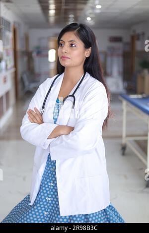 Porträt einer selbstbewussten Oberärztin mit überkreuzten Armen. Glücklicher Arzt in weißem Laborkittel, der im Krankenhausflur steht. Stockfoto
