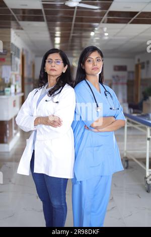 Profilaufnahme einer indischen Ärztin, die hinten an hinten steht. Oberarzt im weißen Anzug und Krankenschwester in blauer Uniform. Stockfoto