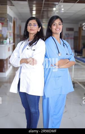 Profilaufnahme einer indischen Ärztin, die hinten an hinten steht. Oberarzt im weißen Anzug und Krankenschwester in blauer Uniform. Stockfoto