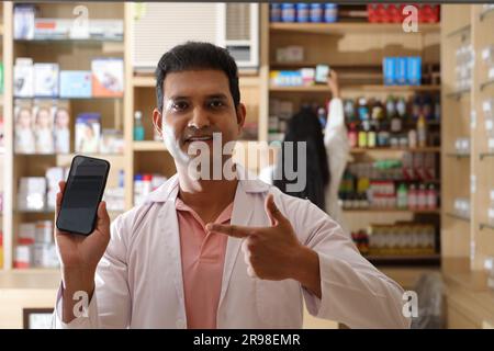 Apotheker, der Kunden in der Apotheke hilft. Zeigen Sie das Smartphone und die mobile App in der Hand. Apotheker-Chemiker Mann in der Apotheke - Drogeriemarkt Stockfoto