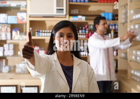 Apotheker, der Kunden in der Apotheke hilft. Mit Daumen nach oben. Apothekerin Chemikerin in Apotheke - Drogeriemarkt Stockfoto