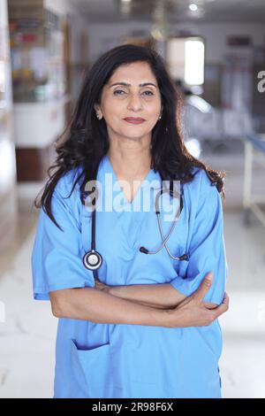 Porträt einer Ärztin mit überkreuzten Armen. Glückliche Krankenschwester in blauer Uniform, die im Krankenhauskorridorhintergrund steht. Vertrauen Stockfoto