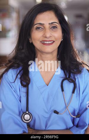 Porträt einer Ärztin mit überkreuzten Armen. Glückliche Krankenschwester in blauer Uniform, die im Krankenhauskorridorhintergrund steht. Vertrauen Stockfoto