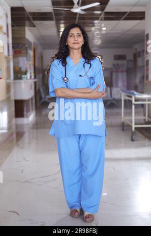 Porträt einer Ärztin mit überkreuzten Armen. Glückliche Krankenschwester in blauer Uniform, die im Krankenhauskorridorhintergrund steht. Vertrauen Stockfoto