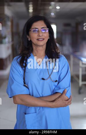 Porträt einer Ärztin mit überkreuzten Armen. Glückliche Krankenschwester in blauer Uniform, die im Krankenhauskorridorhintergrund steht. Vertrauen Stockfoto