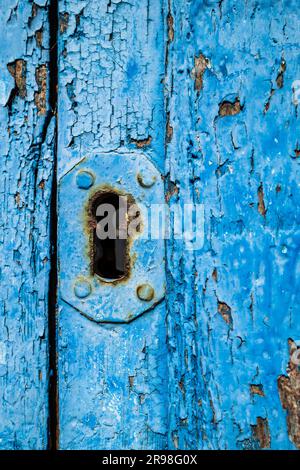 Nahaufnahme des Schlüssellochs in einer altblauen Holztür mit rauer, strukturierter Holzmaserung Stockfoto