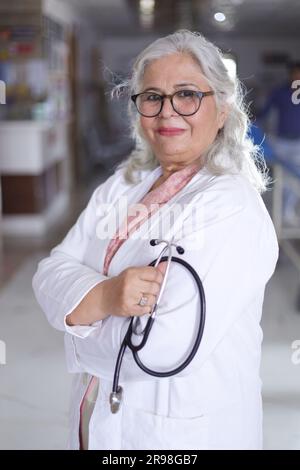 Porträt einer Oberärztin mit überkreuzten Armen im Krankenhauskorridor. Happy Indian Doctor White Laborkittel Stockfoto