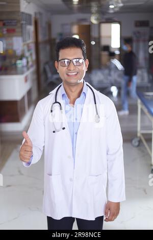 Glücklicher indischer Senior Medical professionell Standbild im Flur des Krankenhauses gekleidet in Peelings und Labormänteln, mit Stethoskopen. Stockfoto
