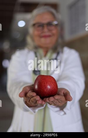 Die Botschaft zu zeigen, um eine bessere Gesundheit und einen sehr gesunden Ernährungsplan zu haben. Attraktive Ärztin mit einem lächelnden weißen Fell und einem Apfel. Stockfoto