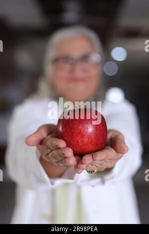 Die Botschaft zu zeigen, um eine bessere Gesundheit und einen sehr gesunden Ernährungsplan zu haben. Attraktive Ärztin mit einem lächelnden weißen Fell und einem Apfel. Stockfoto