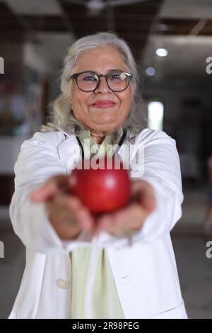 Die Botschaft zu zeigen, um eine bessere Gesundheit und einen sehr gesunden Ernährungsplan zu haben. Attraktive Ärztin mit einem lächelnden weißen Fell und einem Apfel. Stockfoto