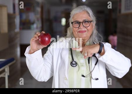 Die Botschaft zu zeigen, um eine bessere Gesundheit und einen sehr gesunden Ernährungsplan zu haben. Attraktive Ärztin mit einem lächelnden weißen Fell und einem Apfel. Stockfoto