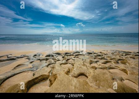 Eine malerische Strandszene mit einer Fülle von großen Felsen, die über den Sandstrand verstreut sind: Stockfoto